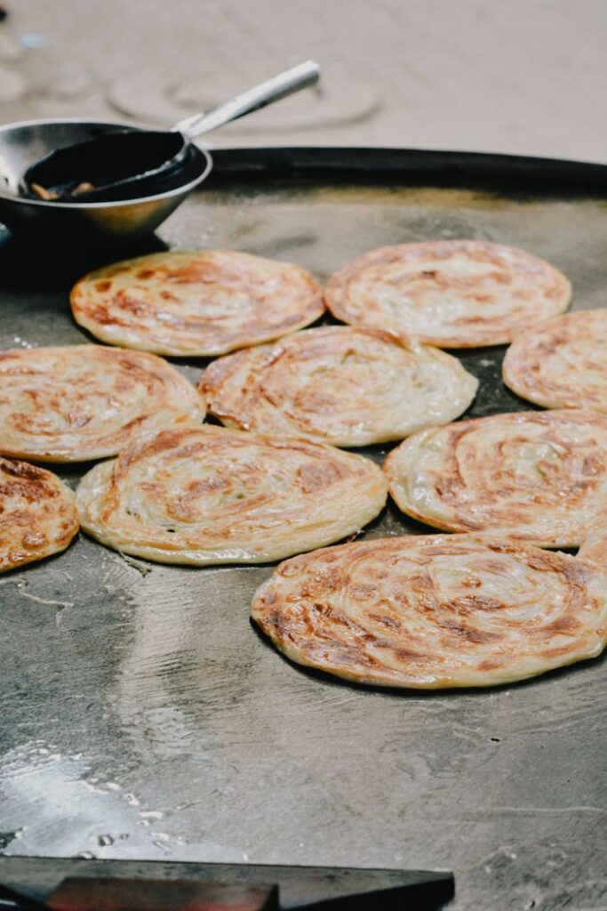 10 Makanan Tradisional Malaysia yang terkenal Delicious traditional parathas sizzling on a tawa, capturing authentic South Asian street food culture.
